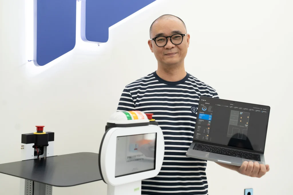 서빙로봇 이리온과 관제시스템 네플러와 함께 환하게 웃고 있는 폴라리스쓰리디 김현대 네플러 그룹장의 모습.